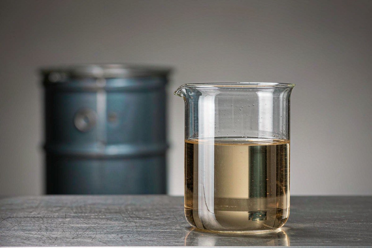 glass beaker of pale amber liquid phenolic novolac epoxy resin YLEP-631 on a stainless laboratory bench with a steel drum behind